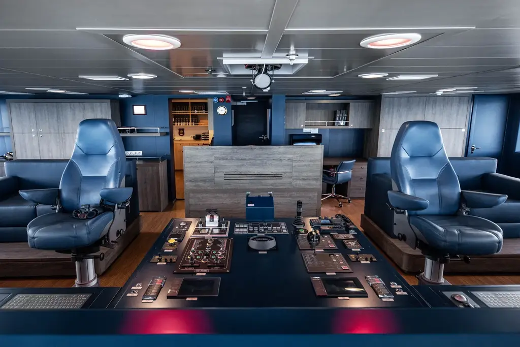 The bridge with two blue helm chairs on either side of a wide central console of controls and screens