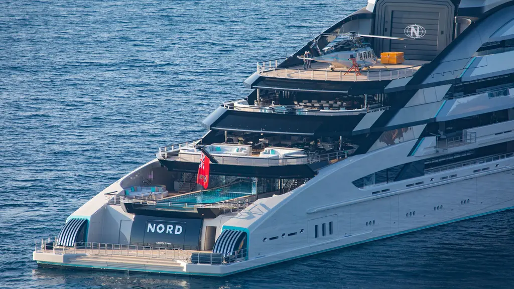 Nord's aft decks from above: a helicopter on the upper-deck helipad in front of the hangar, the pool on the main deck aft and the name on the transom