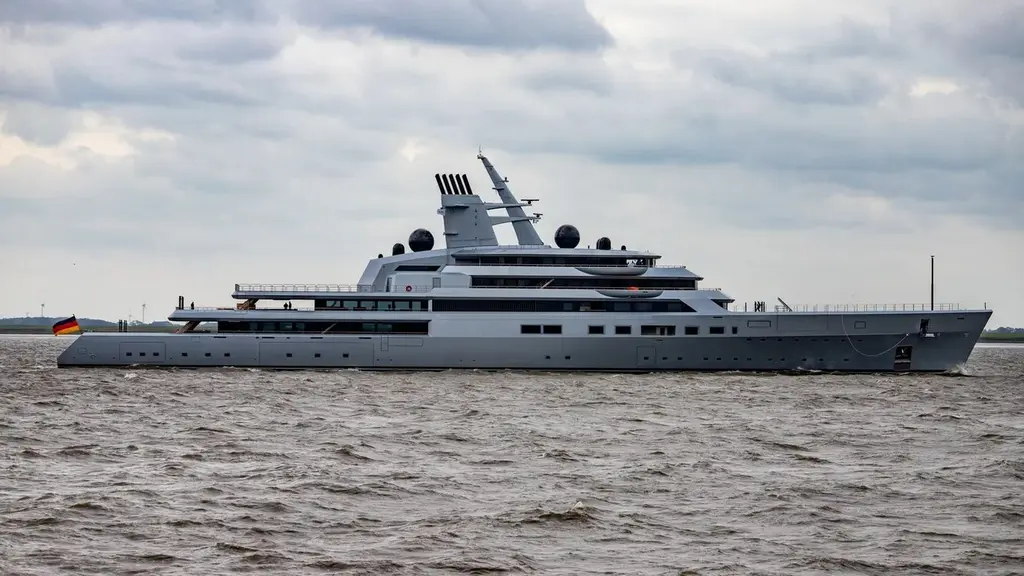 Dragonfly in full profile on a wide brown river under a grey sky, German flag at the stern