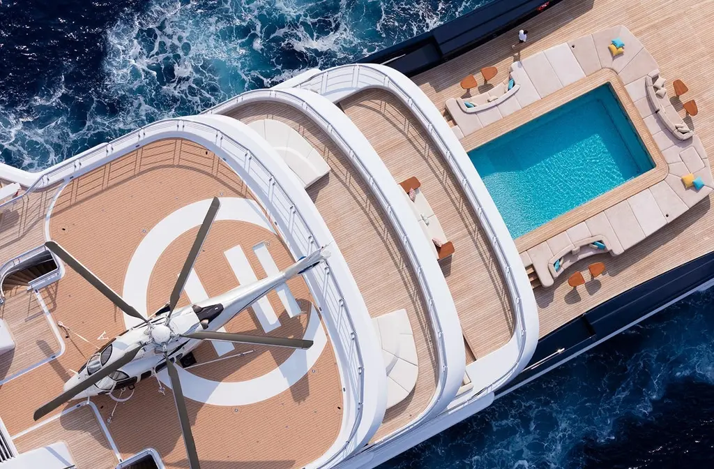 Aerial close-up of the aft helipad with a helicopter parked on the landing circle, above the pool on the deck below