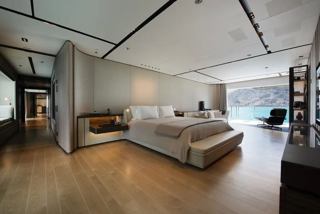 A large stateroom with a pale bed, wooden floor and a glass wall opening to the sea