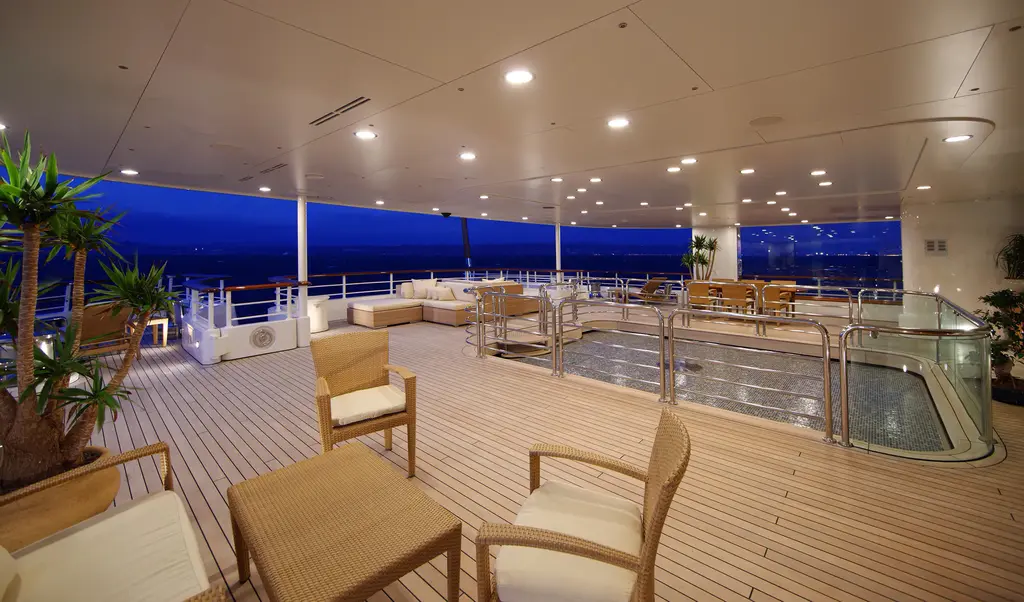 Covered aft deck at dusk with teak floor, wicker chairs and the pool