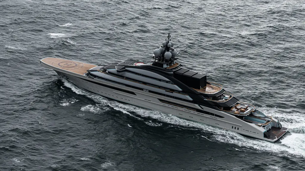 Aerial view of the yacht underway in grey water, the bow helipad forward and the build name Opus on the superstructure