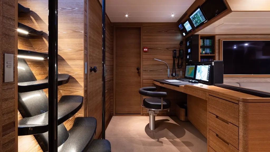 Navigation station with a desk, screens and a helm chair next to a wooden companionway stair