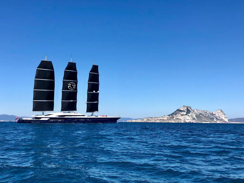 Black Pearl under sail at a distance, with a rocky headland on the horizon