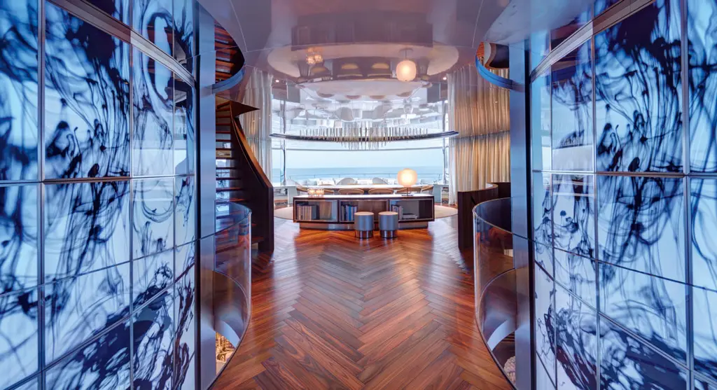 A passage lined with blue abstract video screens leading to a lounge with a herringbone wooden floor