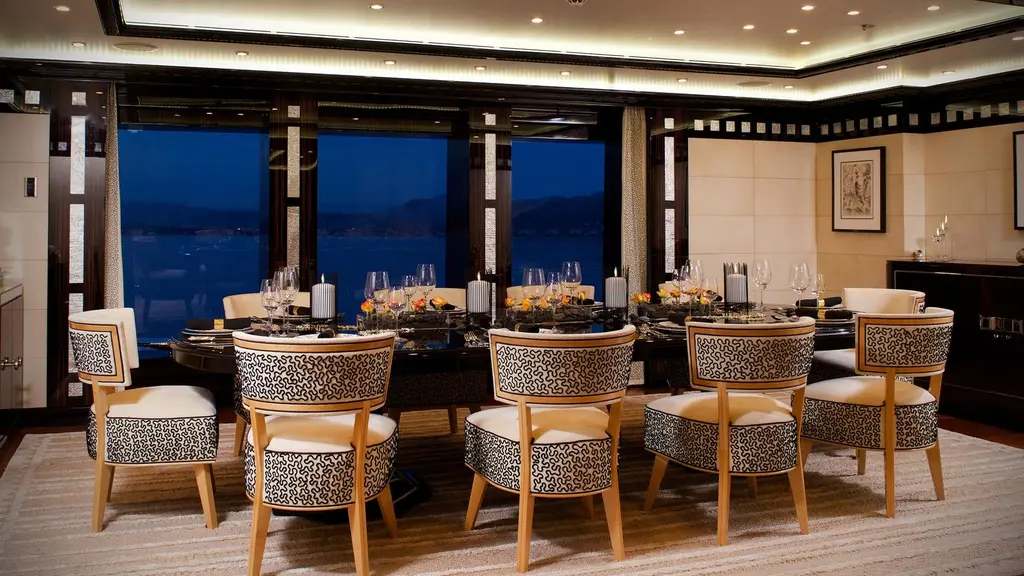 Dining room with a long table, patterned chairs and tall windows at dusk