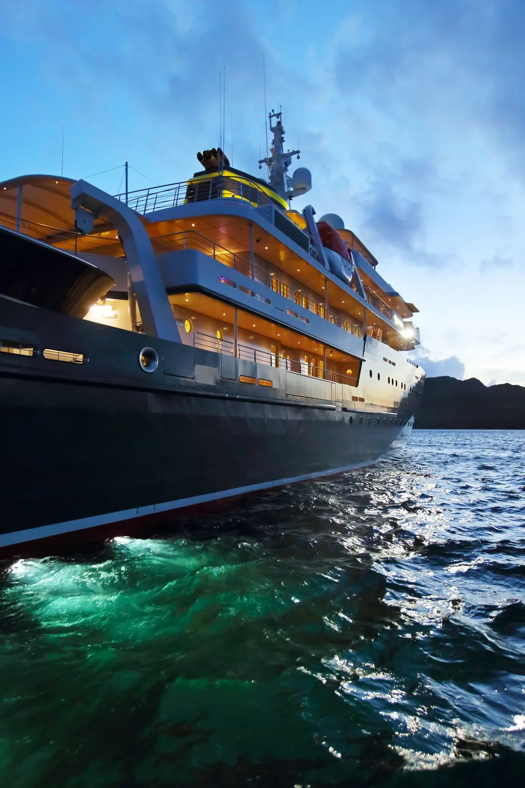Yersin's dark hull at dusk with lit decks above and green underwater lights in the sea alongside