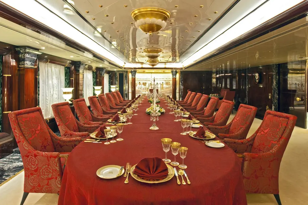 Long dining table laid with red cloths and gold-rimmed glasses, chairs on both sides