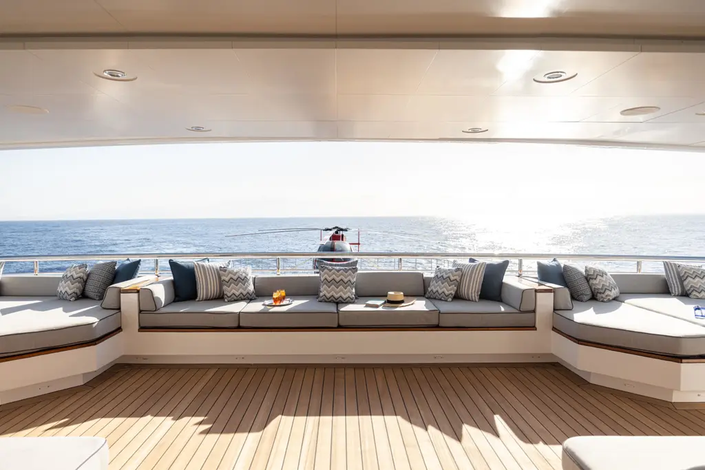 Covered aft lounge with a long sofa, looking out over the helicopter on the deck behind