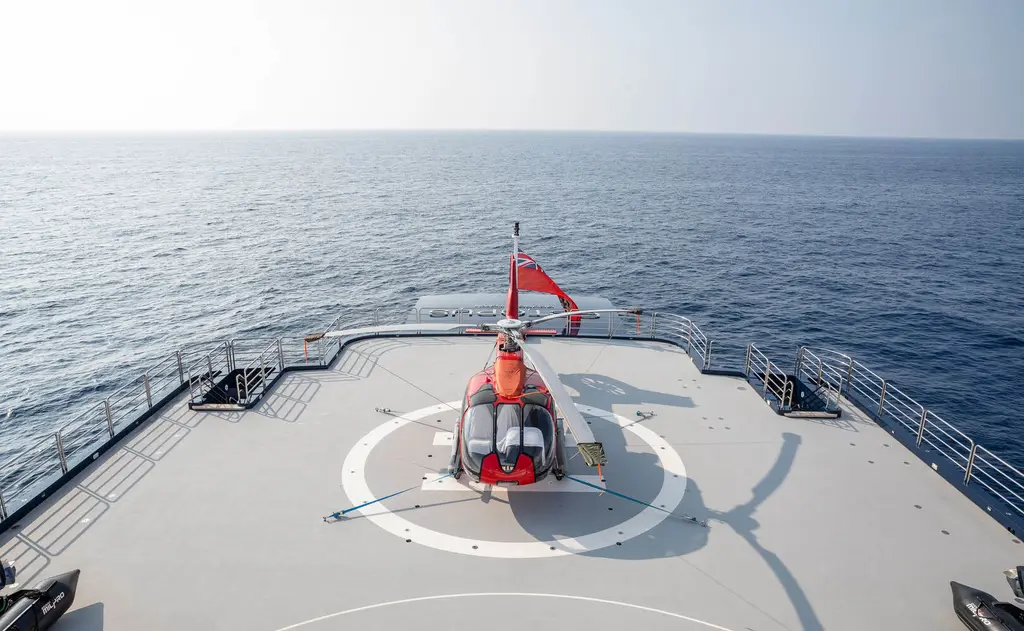 Red and white helicopter parked on a marked helipad at sea, open water to the horizon