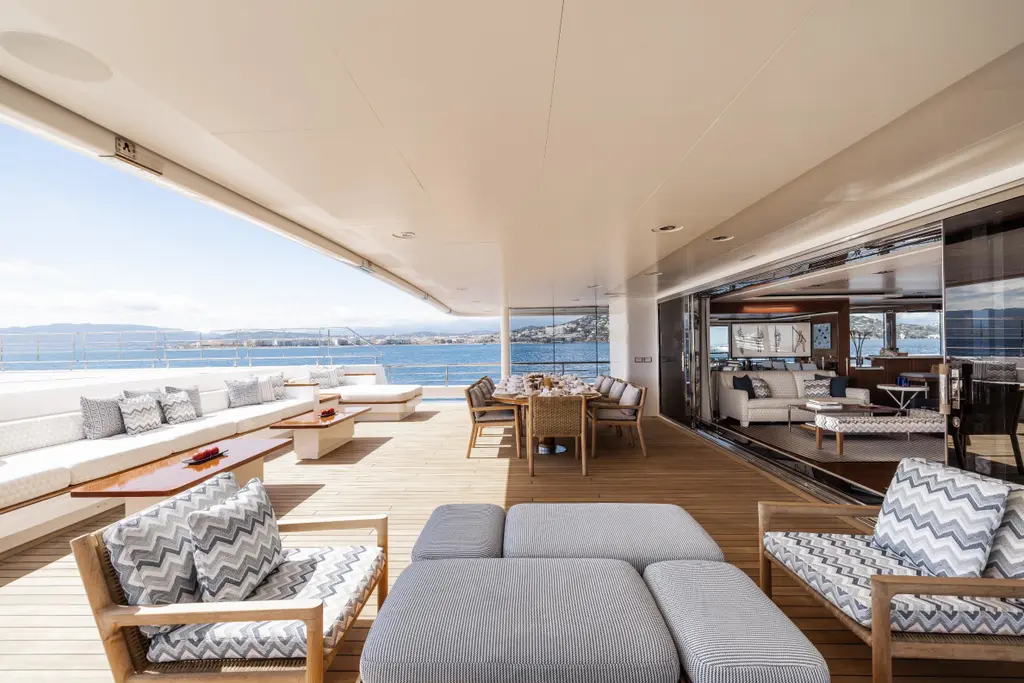 Shaded aft deck with sofas and armchairs, a dining table and glass doors open to the saloon