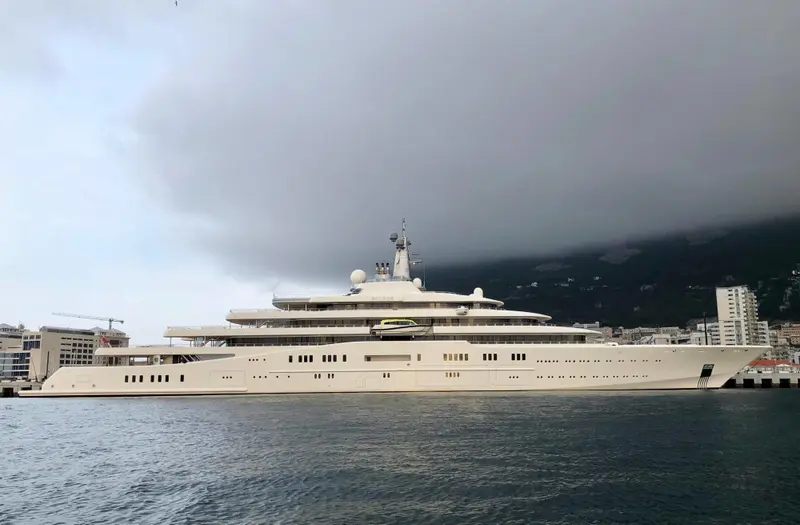 Eclipse moored along a harbour quay under heavy grey cloud, a mountainside behind