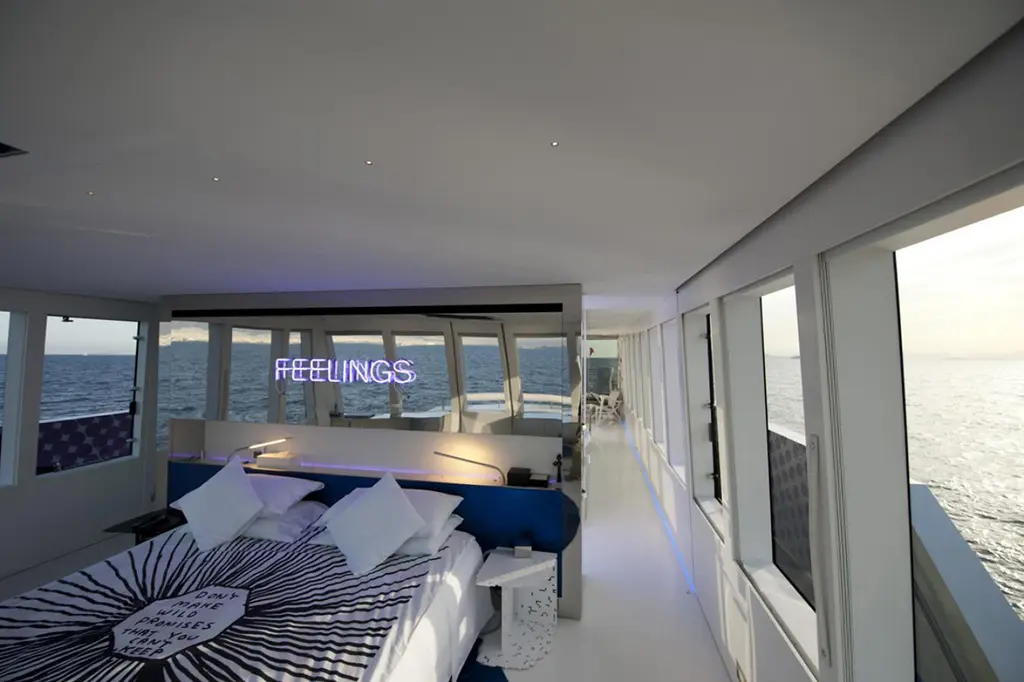 Owner's cabin with a large bed facing forward windows and a purple neon sign reading FEELINGS above the windows