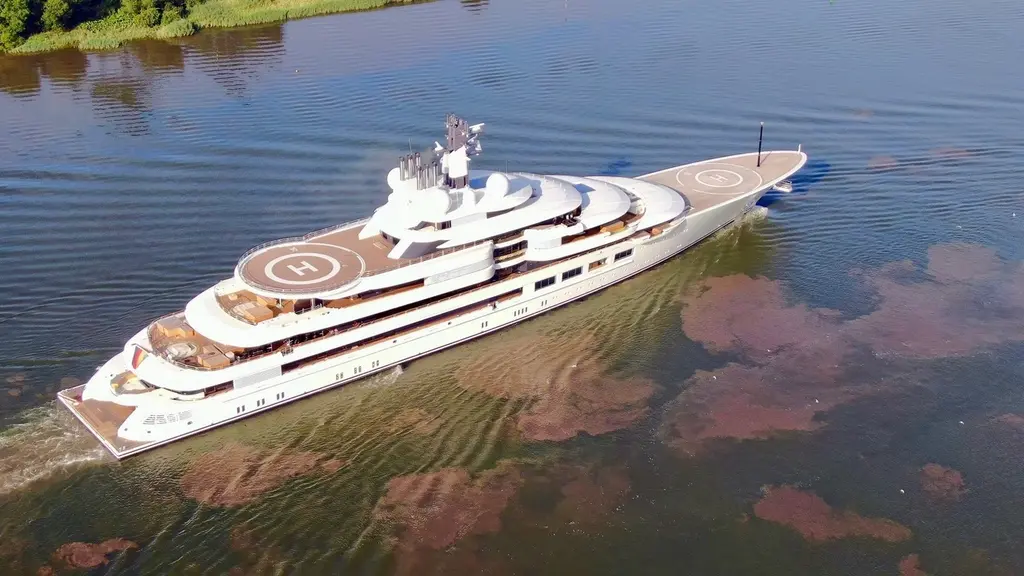 Aerial view of Scheherazade underway on a river, with the bow helipad and the upper-deck helipad marked H
