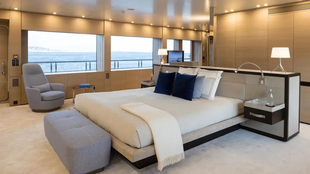 A large cabin with a double bed facing tall windows, a grey armchair and pale oak panelling