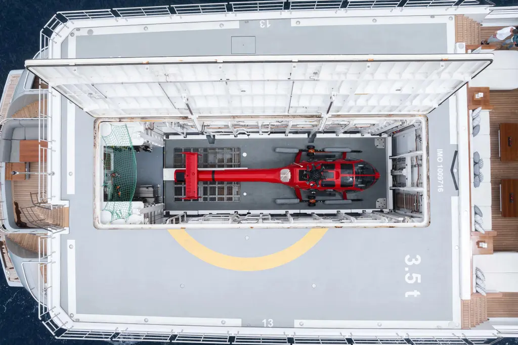 Overhead view of the helideck with its hatch open and the red helicopter lowered into the hangar below