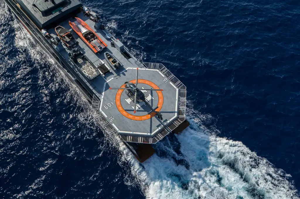 The helipad of Hodor from directly above at speed, an octagonal deck with an orange circle and H marking, a grey helicopter on it and a white wake behind