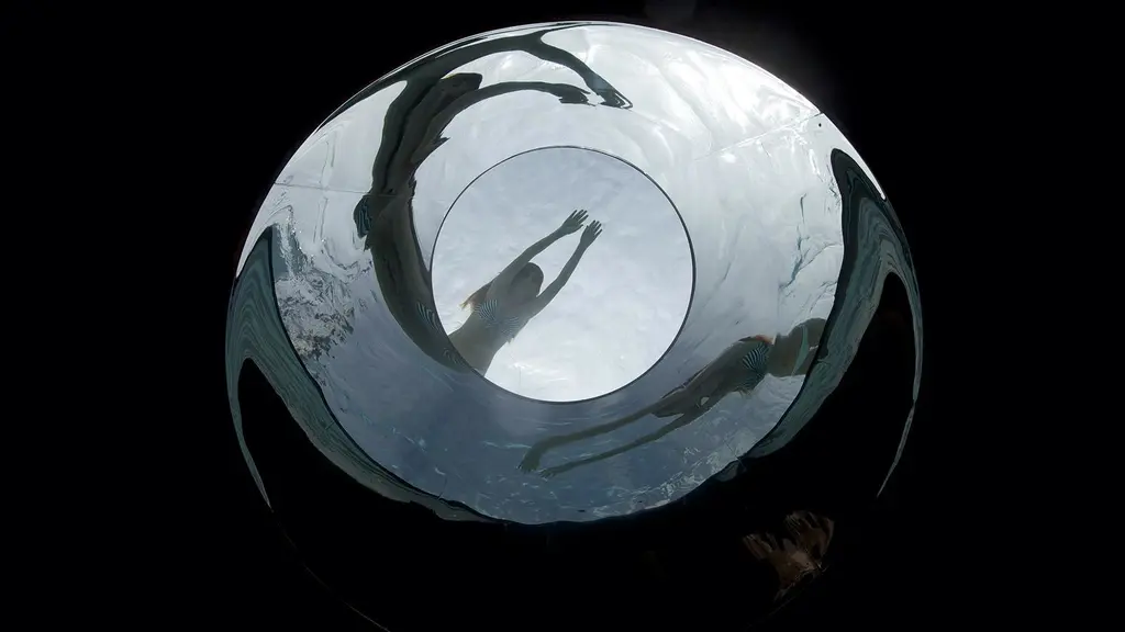 Swimmers seen from below through the round glass base of a pool