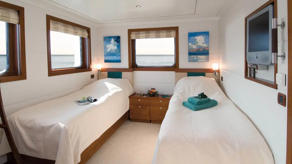 Twin guest cabin with two single beds under three windows, before the 2021 refit