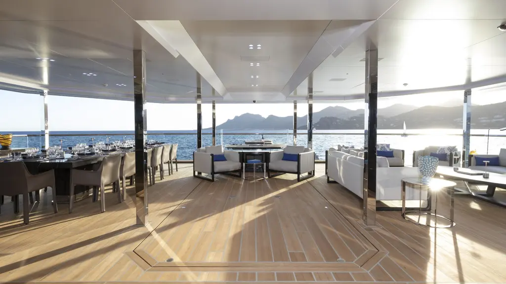 The winter garden with its glass walls open to the sea and the mountains beyond, with sofas and a dining table on a pale wooden floor