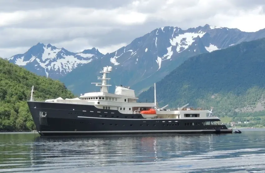 Legend at anchor in a calm fjord below steep green slopes and snow-capped mountains