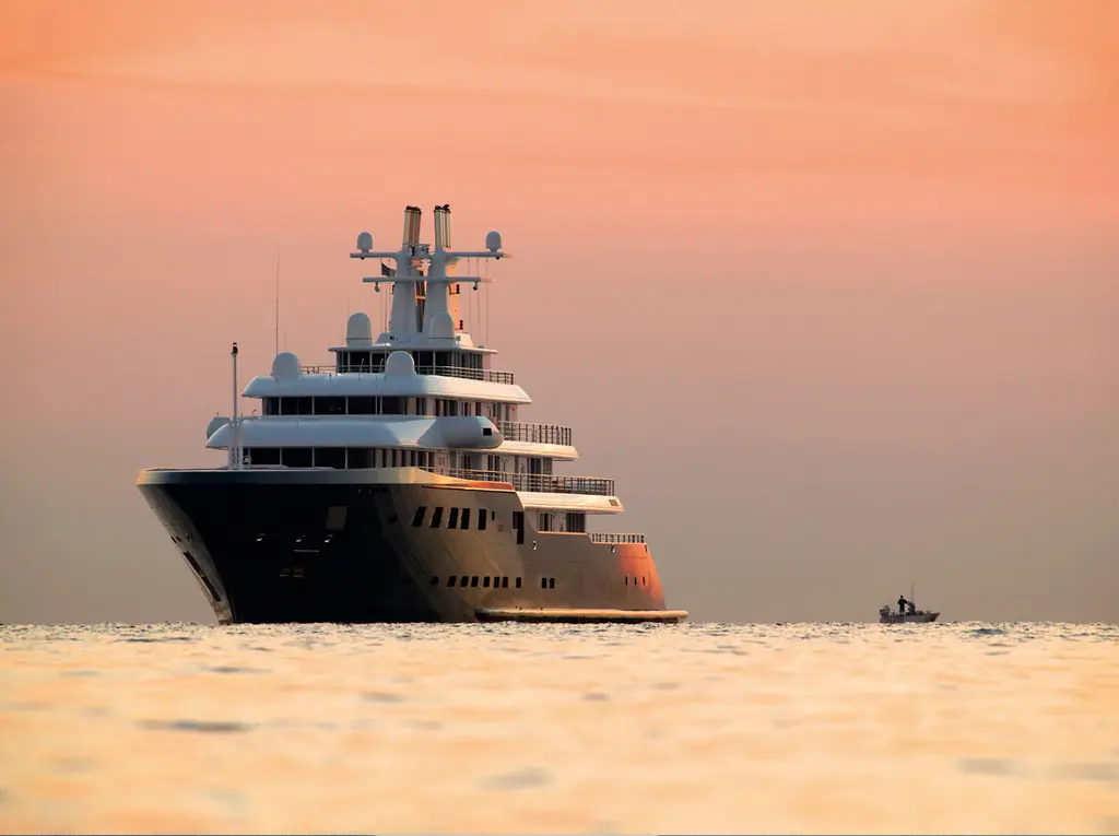 Ice at anchor at sunset seen bow-on, with a small tender nearby on calm orange water