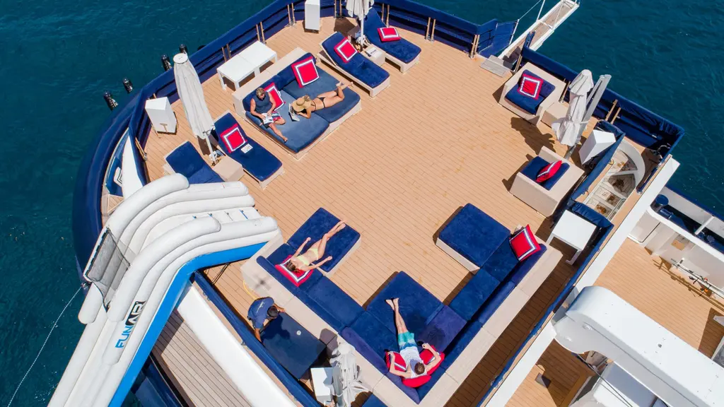 Aft sun deck of Arctic from above: teak deck, navy loungers with red cushions and the top of a water slide