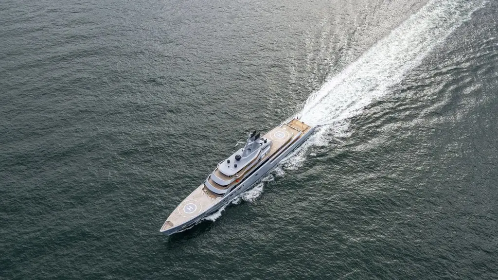 Aerial view of Dragonfly under way with a long white wake, helipads visible on the foredeck and aft deck