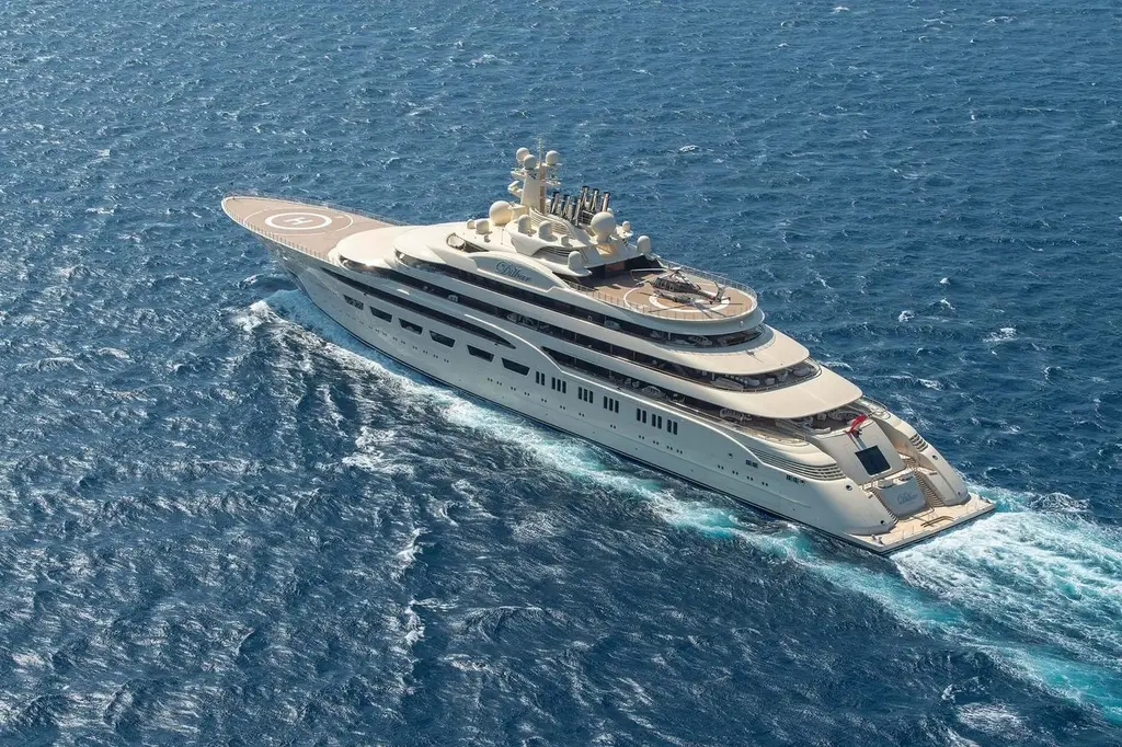 Aerial three-quarter view of Dilbar underway from astern, with the name on the superstructure and a helicopter on the aft helipad
