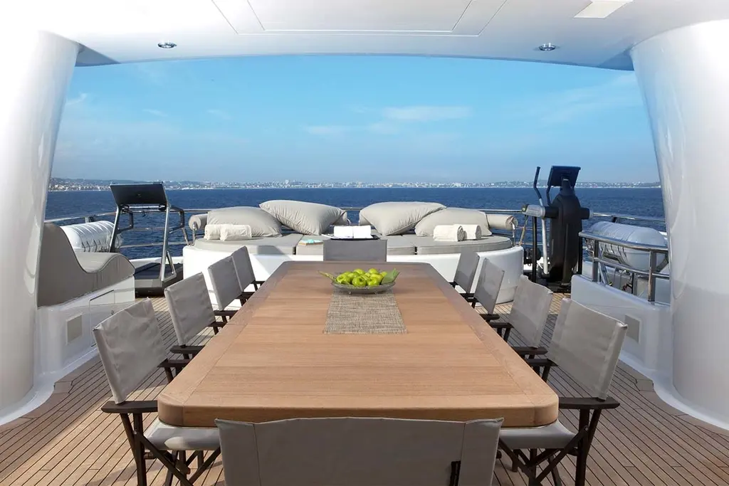Outdoor dining table on a teak deck, with a lounge and gym equipment behind