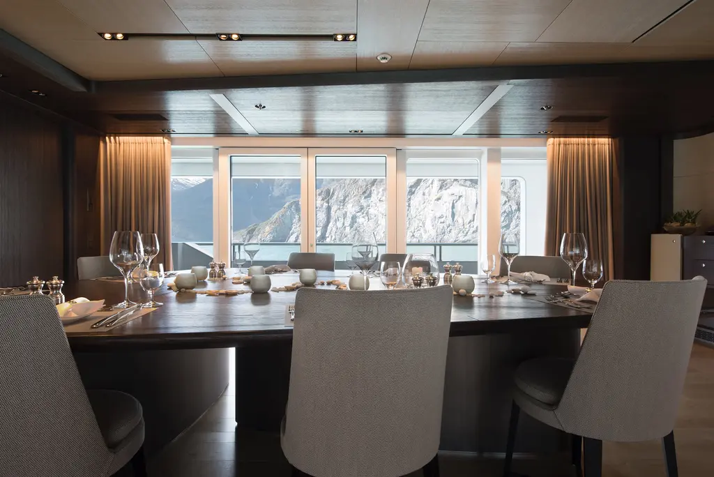 A dining table laid for a meal in front of floor-to-ceiling windows with a glacier view