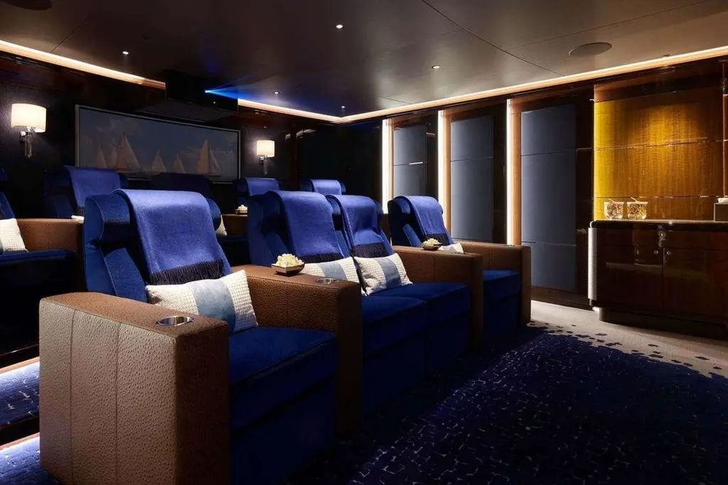 Cinema with tiered rows of blue velvet recliners and a bar along the side wall