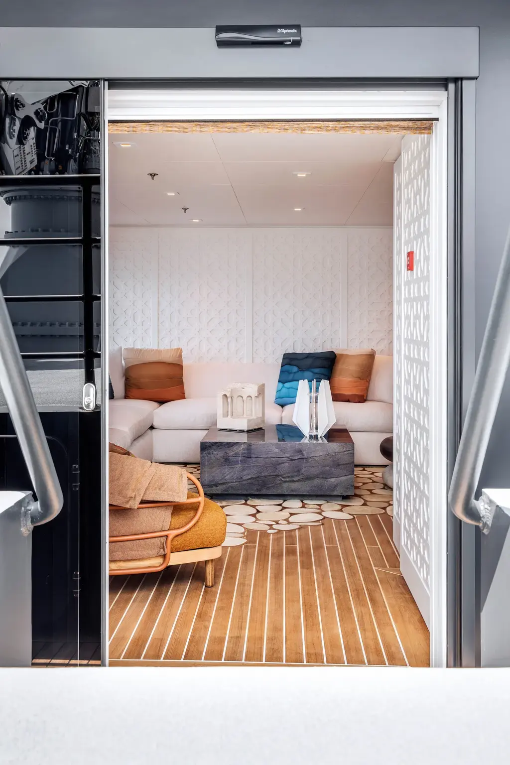 A view through a sliding door from a grey stairway into the white guest lounge with its fretwork panels and sofa