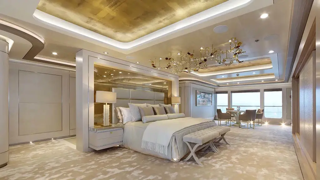 Owner's stateroom with a large bed, gold-leaf ceiling and a small dining table by the windows
