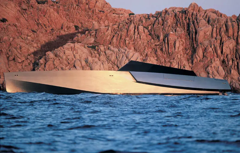 Side profile of the Wallypower 118, a low wedge-shaped hull in front of red rock cliffs