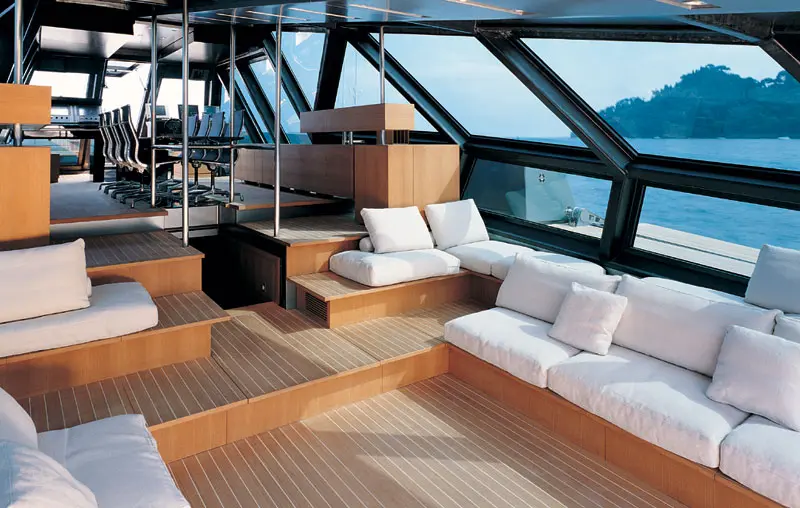 Saloon under the glass deckhouse with white sofas, wooden floor steps and a sloping dark frame of windows