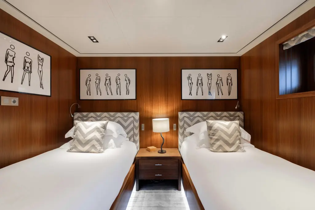 Guest cabin with two single beds and framed drawings on wood-panelled walls