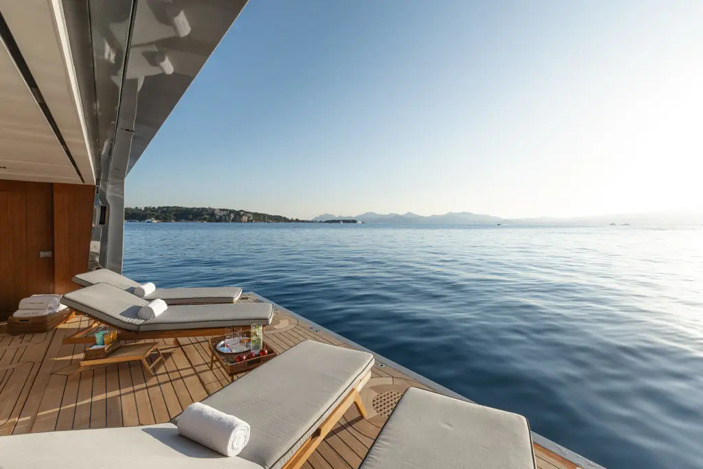 Sun loungers on a teak terrace at the bow, with the sea and the coast ahead