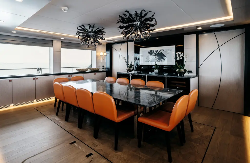 Formal dining table for twelve with orange leather chairs under two sculptural chandeliers