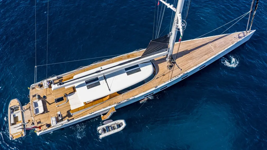 Overhead view of Canova lying still with her mainsail stowed and two tenders alongside, showing the flush teak deck and coachroof