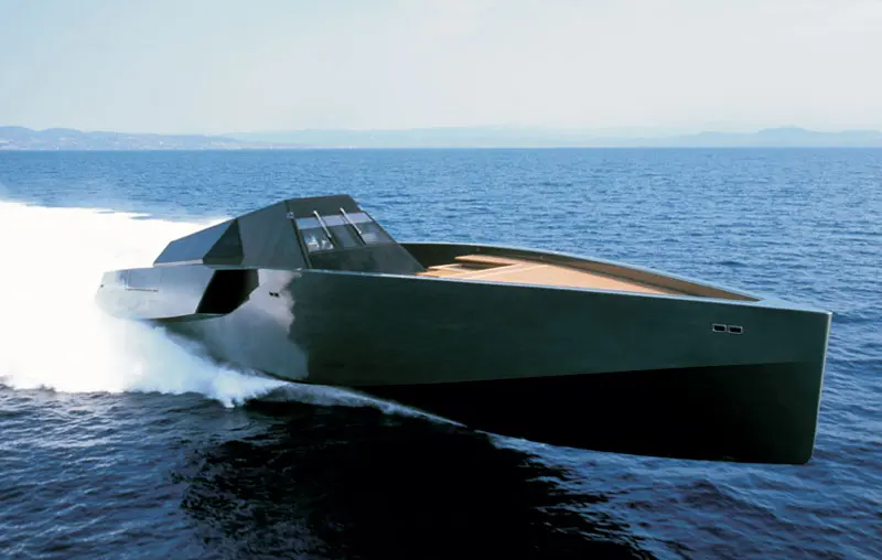 The Wallypower 118 running fast, three-quarter view from the bow, spray off the angular hull and a coast on the horizon