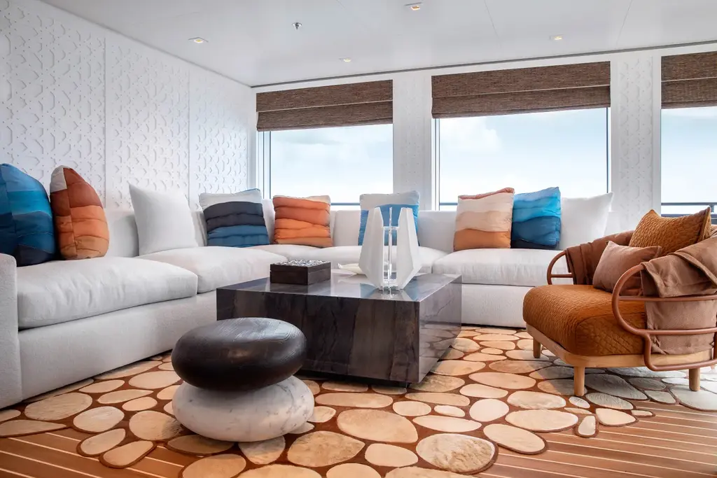The guest lounge with white fretwork wall panels, a white sectional sofa with blue and orange cushions, a dark stone coffee table and a rug of wooden discs
