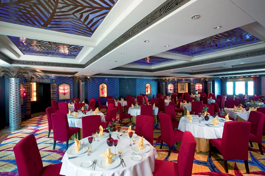 Dining room with round tables laid with white cloths, red chairs and a coffered ceiling