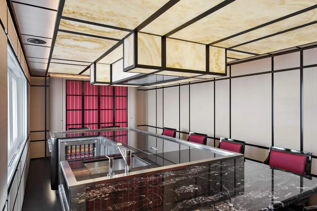 Dining room built around a central teppanyaki grill with red-upholstered chairs and lacquer panels
