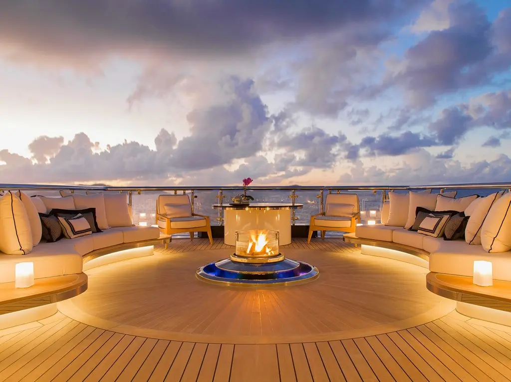 Curved outdoor sofas around a lit fire pit on the aft deck at dusk