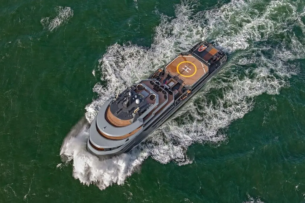 Ragnar seen from directly above, cutting through green water with a wide white wake, with the helipad, sundeck and teak decks visible