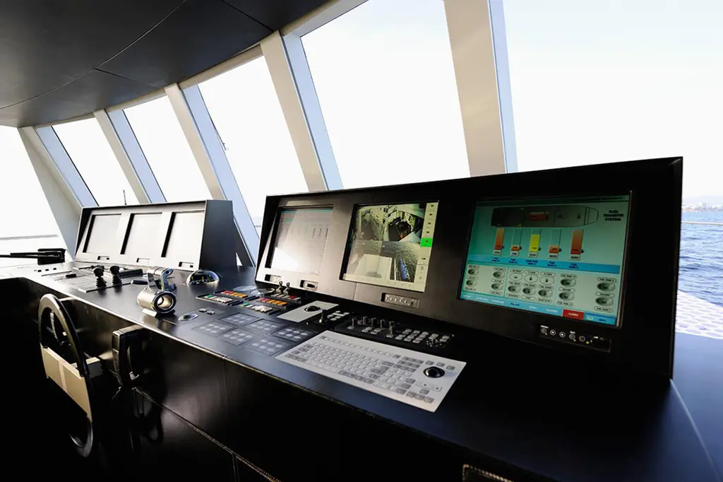 Bridge console with a wheel, keyboards and three screens under tall sloping windows