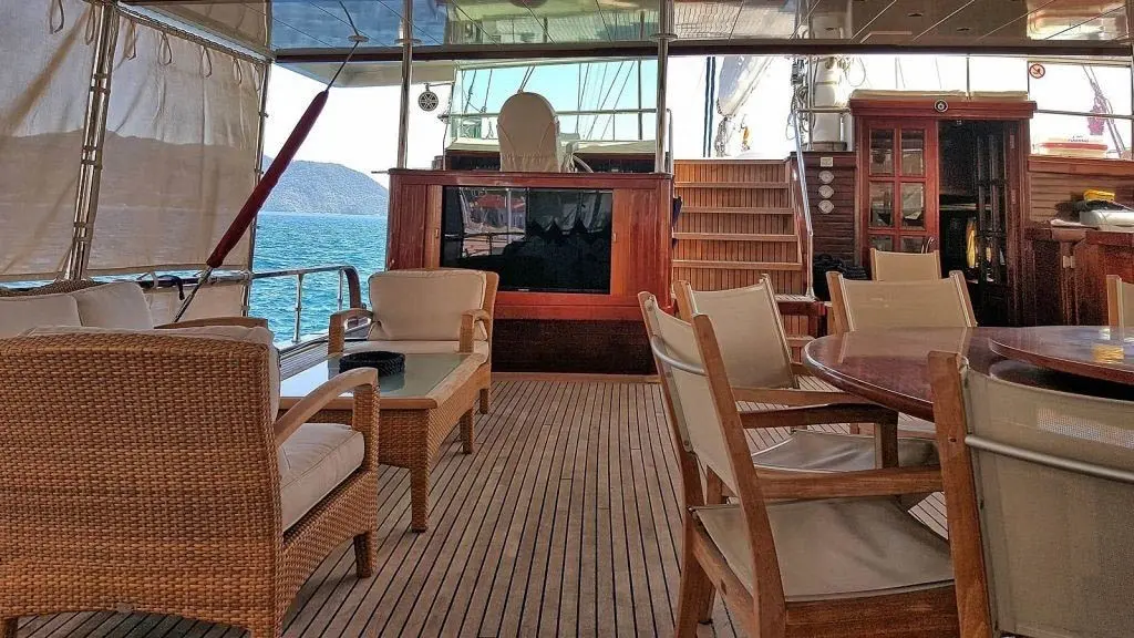 Shaded aft deck with wicker armchairs, a dining table and the helm station behind