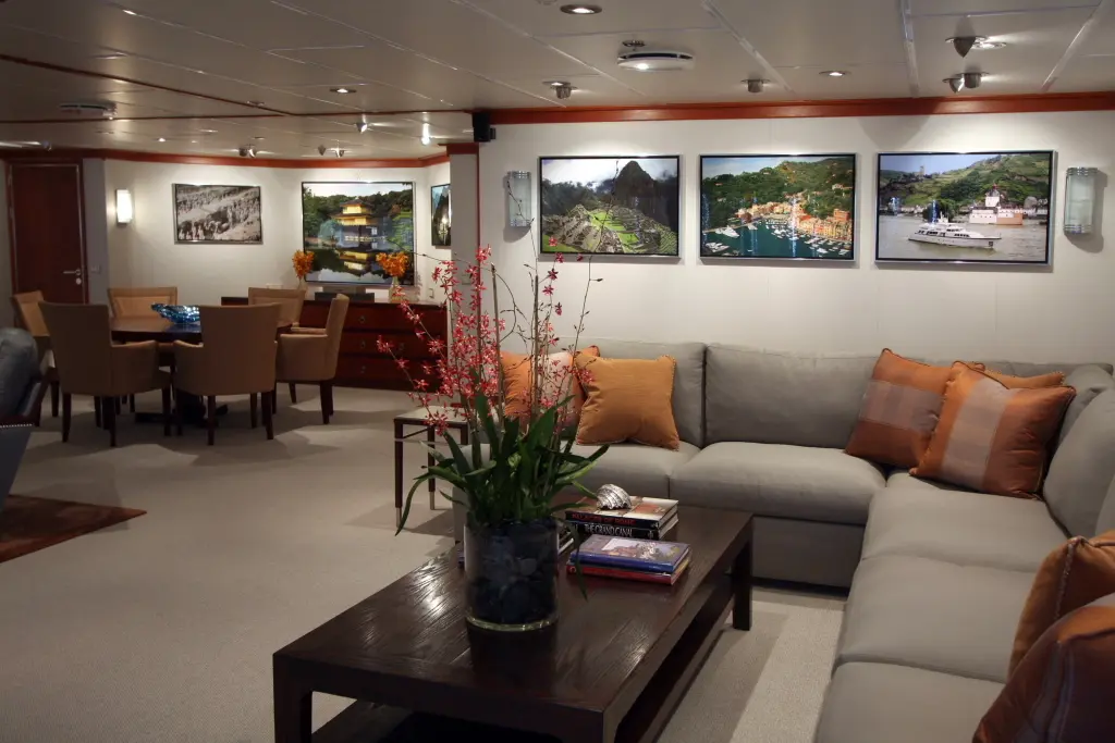 Main saloon of Silver Cloud with a grey sectional sofa, wood joinery and framed photographs on the walls